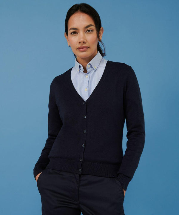 A person wearing a light blue Henbury HB726 button-down shirt underneath a dark blue cardigan stands against a blue background.