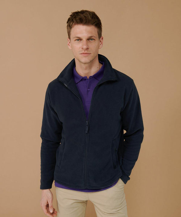 A person wearing a dark navy Henbury HB850 jacket over a purple shirt stands against a beige background.