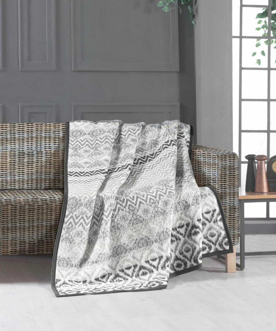 A woven rattan "HL210" sofa by Home & Living with a patterned black-and-white blanket draped over its arm, situated next to a window with some potted plants visible.