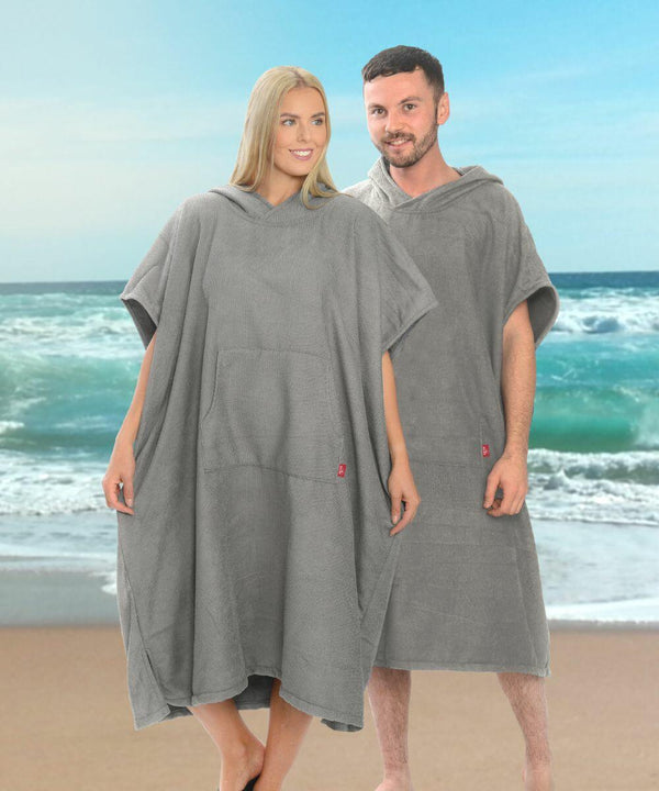 Two people stand on a beach wearing gray Home & Living HL211 hooded poncho towels, with the ocean and sky in the background.