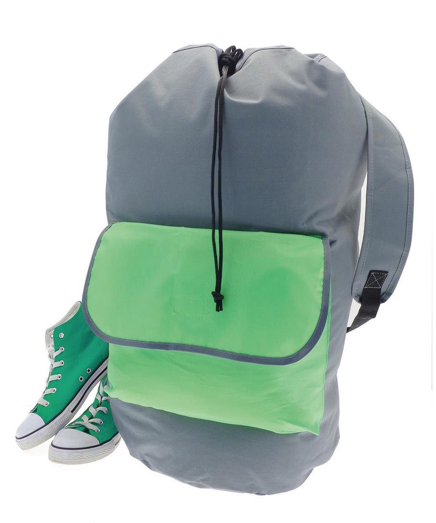 A large grey Home & Living Laundry rucksack with a green front pocket and black drawstring stands upright beside green trainers with white soles and laces, all set against a white background.