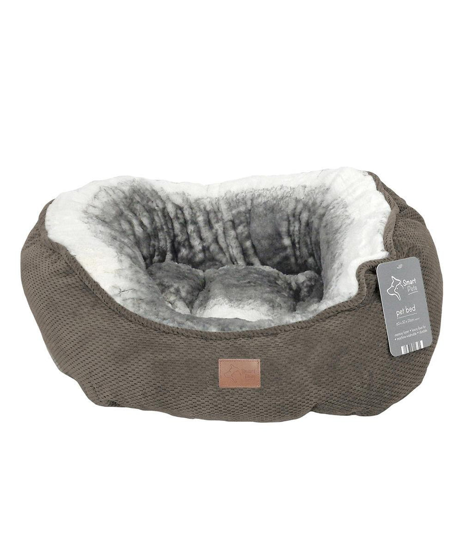 A round, grey Dog Bed featuring a soft, plush white and grey interior. The textured outer fabric includes an attached label with product information. The empty bed is displayed on a white background.