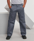 Person wearing Russell J001M gray cargo pants and black shoes stands with hands in pockets in front of geometric gray shapes.