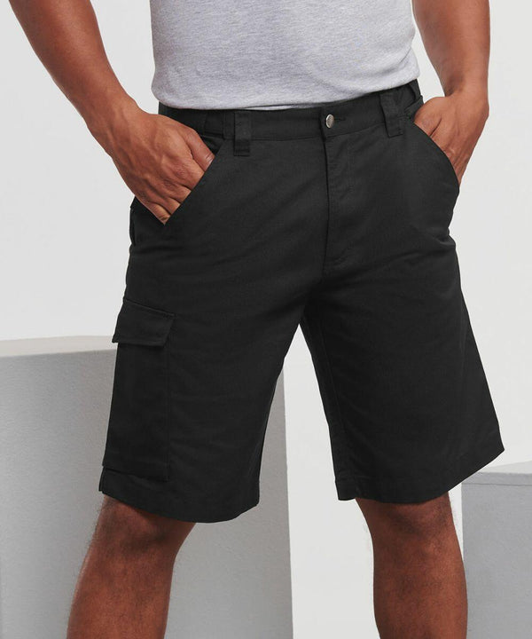 A person wearing black Russell J002M cargo shorts and a light gray shirt stands with hands in pockets, showcasing the shorts' front pockets and side cargo pocket.