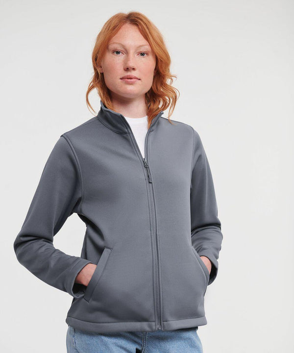 Person with red hair wearing a grey Russell J040F zip-up jacket, standing with hands in pockets, and looking ahead.