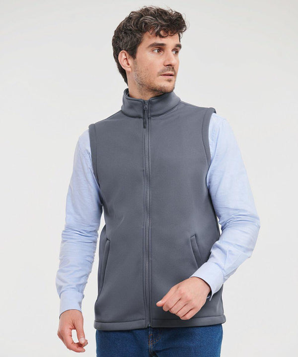 A man with curly hair is wearing a light blue shirt and a gray Russell J041M vest while looking to the side. He has his left hand partially in his pocket.