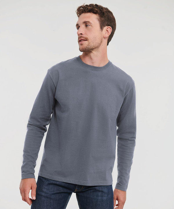 A man with short hair and a beard is wearing a grey long-sleeve J180L by Russell and jeans, looking to his left against a plain background.