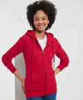 A person wearing a red Russell J266F hoodie over a white t-shirt, standing with hands in the hoodie pockets against a plain background.