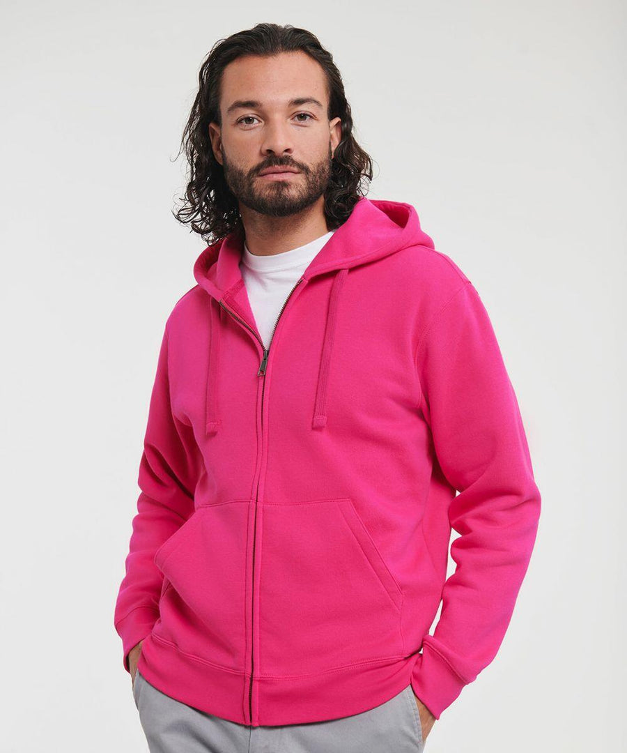 A person with long hair and a beard wearing a bright pink Russell J266M hooded sweatshirt with a zipper stands facing the camera.