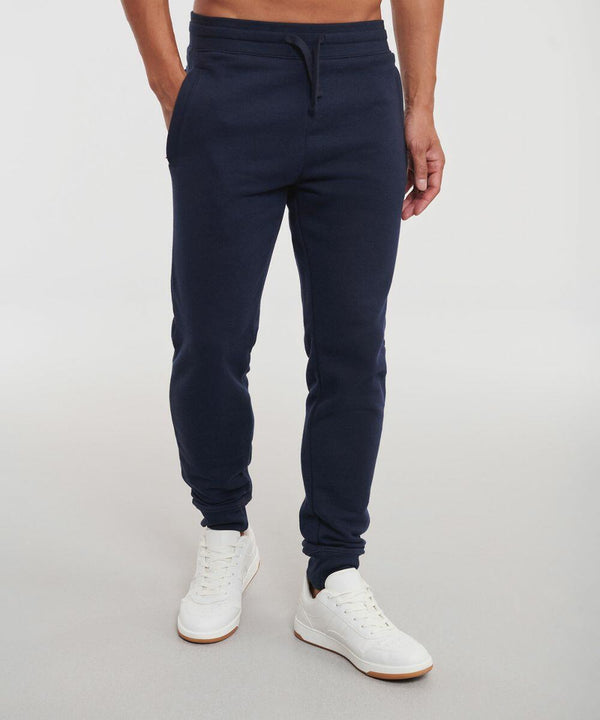 A person wearing navy blue jogger pants and white sneakers is standing on a plain background. Their upper body, dressed in a Russell J268M, is not fully visible.