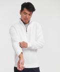 A person wearing a white Russell J270M quarter-zip sweatshirt adjusts the sleeve of their left arm. The background is plain white.