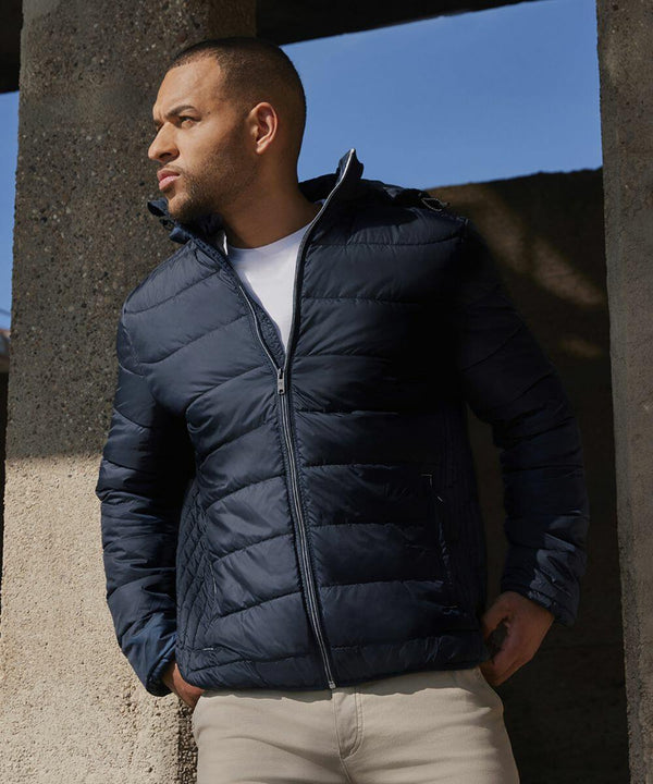 A man wearing a dark blue Russell J440M puffer jacket and beige pants stands outdoors, leaning against a concrete structure and looking to the left.