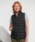 Person with red hair wearing a grey J441F T-shirt under a black puffer vest, standing against a plain background.