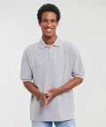 Smiling person wearing a light gray J539M polo shirt by Russell and blue jeans, standing against a plain background.