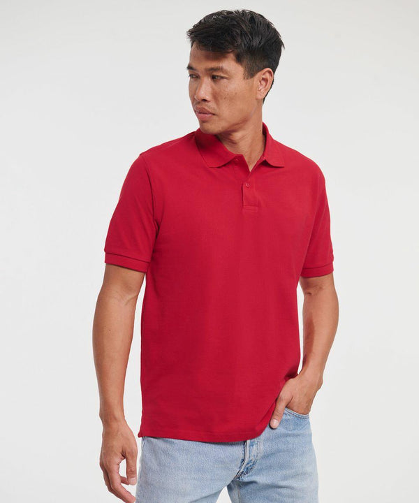 A person wearing a red J569M polo shirt by Russell and light blue jeans stands against a plain background, looking to the side.