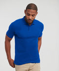 A man wearing a blue Russell J570M and beige pants stands against a plain background, looking down with his right hand in his pocket.