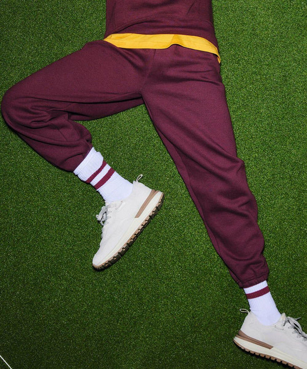 Person wearing maroon Russell J750B sweatpants, a yellow T-shirt, white socks with maroon stripes, and white sneakers lying on green grass.