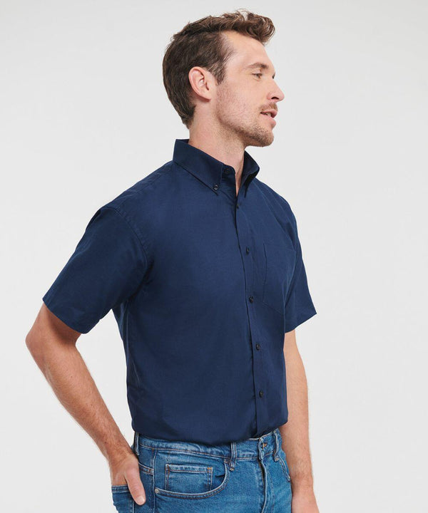 Man wearing a navy blue Russell J933M short-sleeve button-up shirt and blue jeans, standing with one hand in his pocket, looking to the side.