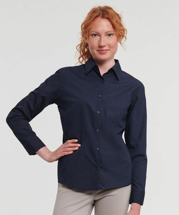 A person with red hair wearing a long-sleeve, dark blue button-up Russell J934F and light-colored pants poses with one hand on their hip against a plain background.
