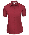 A short-sleeve, button-up shirt in red, featuring a classic collar and a chest pocket, from the Russell Collection's J935F line, is displayed against a white background.