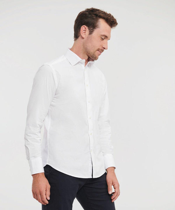 A man in a white long-sleeve J946M button-up shirt by Russell and dark pants stands against a plain background, looking down.
