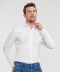 A man in a white Russell J960M button-up shirt and blue jeans adjusts his collar while looking slightly upward.