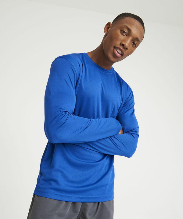 A person wearing a long-sleeved blue AWDis Just Cool JC002 shirt and gray pants stands against a plain background with their arms crossed.