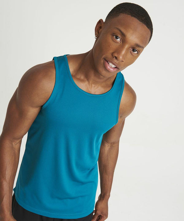 A man in an AWDis Just Cool JC007 teal sleeveless shirt with a slight smile, tilting his head, stands against a plain white background.