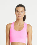 A woman with long hair tied back wearing a bright pink sports bra (JC017 by AWDis Just Cool), standing against a plain white background.