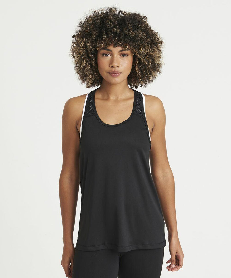 Woman with curly hair wearing a black JC027 tank top by AWDis Just Cool stands against a plain white background, looking directly at the camera.