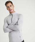A man in a light gray AWDis Just Cool JC030 long-sleeve athletic top with a half-zipper stands with arms crossed against a plain white background.