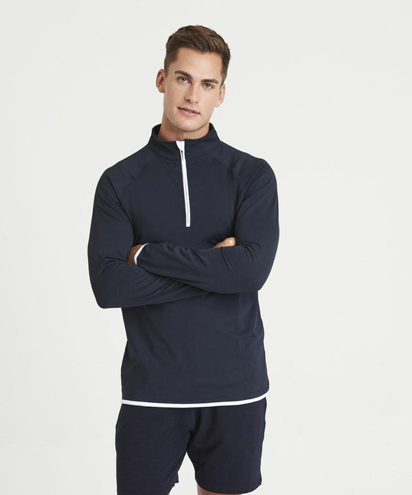 A man stands against a plain background, wearing an AWDis Just Cool JC031 navy long-sleeve half-zip pullover and navy shorts with his arms crossed.