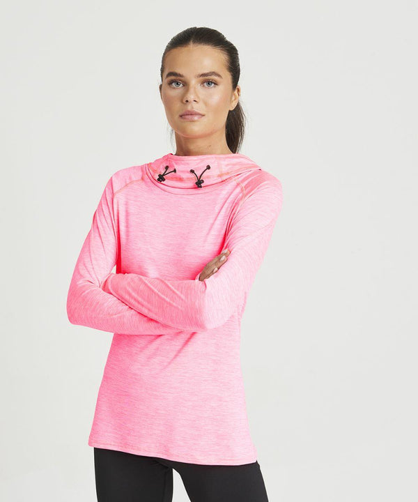 A woman stands with arms crossed, wearing an AWDis Just Cool JC038 bright pink long-sleeve top with a hood and black drawstrings, and black pants, against a plain white background.