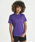A person with curly hair is standing against a plain white background wearing an AWDis Just Cool JC045 and black shorts.