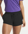 A person wearing an AWDis Just Cool JC074 purple shirt and black shorts with hands partially in pockets.