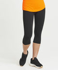 A person wearing black leggings, black sneakers, and an orange **JC086 by AWDis Just Cool** stands against a white background.