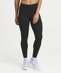 Person wearing AWDis Just Cool JC087 black leggings and lavender sneakers stands against a white background. Their left hand rests on their thigh.