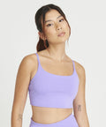 A person with long hair in a JC217 tank top and matching bottoms by AWDis Just Cool stands against a white background. They have tattoos on their arms.