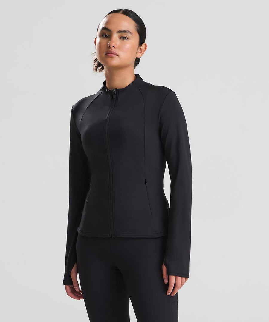 A woman stands against a plain background wearing the AWDis Just Cool Women's recycled tech-zip jacket in black, paired with matching black trousers; her hair is pulled back as she looks straight ahead.