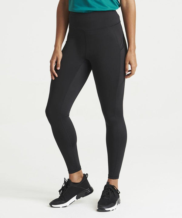A person wearing black JC287 leggings, black sneakers, and a green top from AWDis Just Cool stands against a plain white background. The image shows them from the neck down.