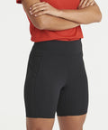 Person wearing a red shirt and black bike shorts standing with their arms crossed. The AWDis Just Cool JC288 shorts have side pockets.