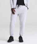 Wearing AWDis Just Cool Adapt fleece joggers in light grey with a matching jacket and black trainers, a person stands against a plain background, left hand in pocket and upper face not visible.