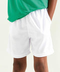 Child wearing a green shirt and AWDis Just Cool JC80J white athletic shorts, with their hand in the pocket of the shorts.