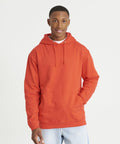 A person wearing an AWDis Just Hoods JH001 hoodie and light jeans stands against a plain white background, smiling with one hand in the hoodie pocket.