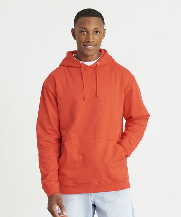 A person wearing an AWDis Just Hoods JH001 hoodie and light jeans stands against a plain white background, smiling with one hand in the hoodie pocket.