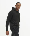 A person wearing a black AWDis Just Hoods JH011 hoodie and black pants stands against a plain white background.