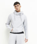 A man wearing an AWDis Just Hoods JH021 light gray hoodie and matching sweatpants stands against a plain white background, posing with one hand in his pocket.
