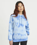 A person with long hair wears a blue tie-dye AWDis Just Hoods JH022 and black pants, standing against a plain white background.