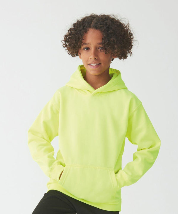 A child with curly hair wearing a neon yellow AWDis Just Hoods JH04J and black pants stands against a plain white background with hands in hoodie pockets.