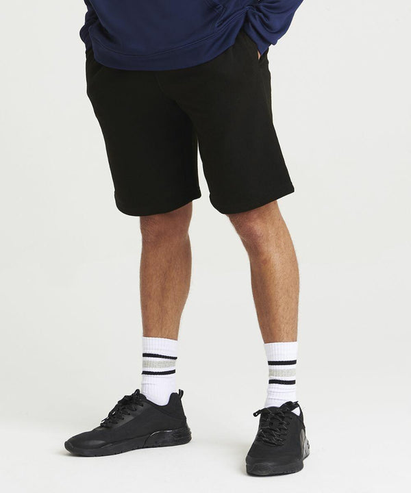 A person wearing black shorts, black sneakers, white socks with black stripes, and a navy JH080 from AWDis Just Hoods, standing against a plain white background.